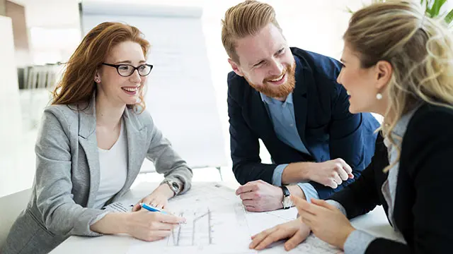 Tre kollegor sitter runt ett bord och ler stort