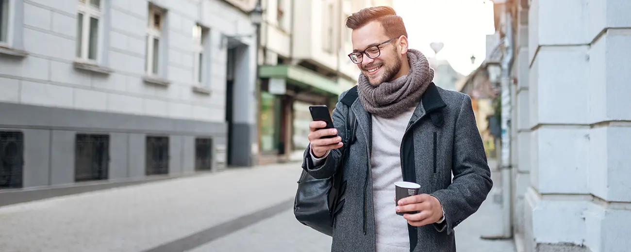Person står utomhus och tittar i sin telefon