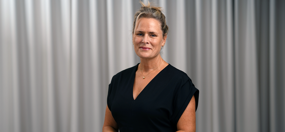 Malin Edlund, psykolog, står svartklädd och tittar leende in i kameran