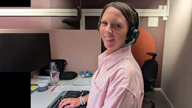 Anna Ekholm Svensson, kundservicemedarbetare, står vid sitt skrivbord och ler mot kameran