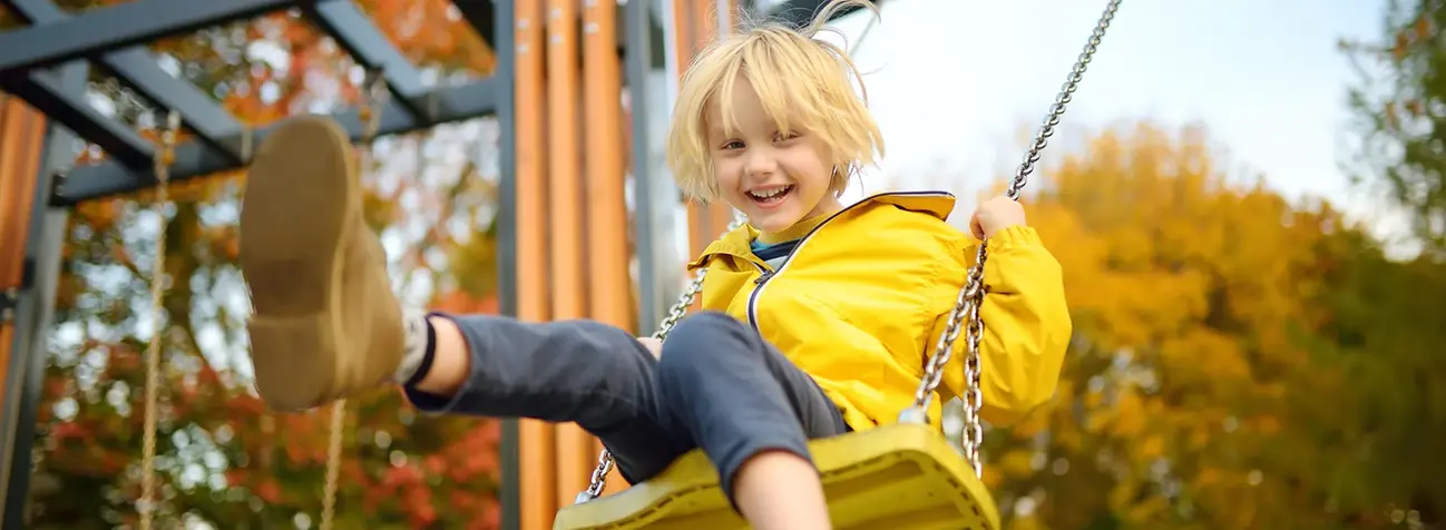 En pojke i gul vidjacka gungar och ser glad ut.