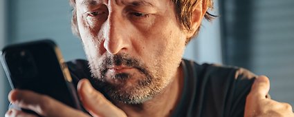 Trött man med skägg i t-shirt tittar in i sin telefon